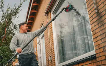 Fönsterputsare med teleskopskaft putsar ett fönster på en tegelvilla
