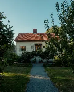 Vit villa med tegeltak bakom en grusgång och gröna träd