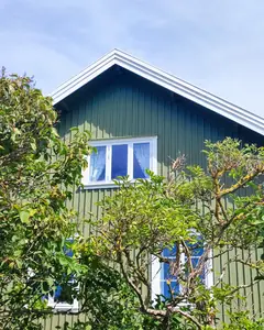 Grönt trähus med vita fönster bakom lummiga träd