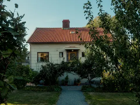 Vit villa med tegeltak bakom en grusgång och gröna träd