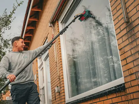 Fönsterputsare med teleskopskaft putsar ett fönster på en tegelvilla